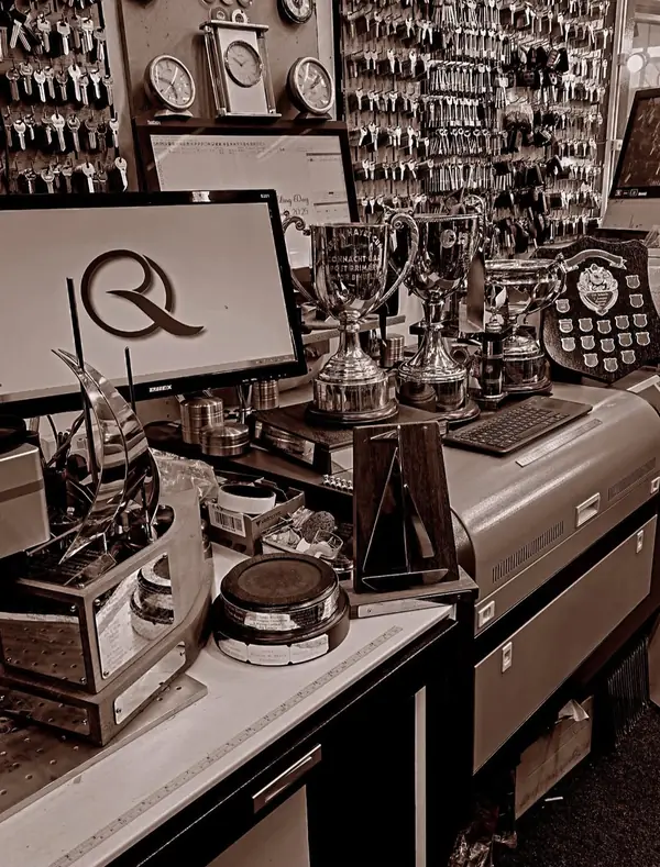 The workbench in black and white, with trophies, the key wall and the shop logo on screen